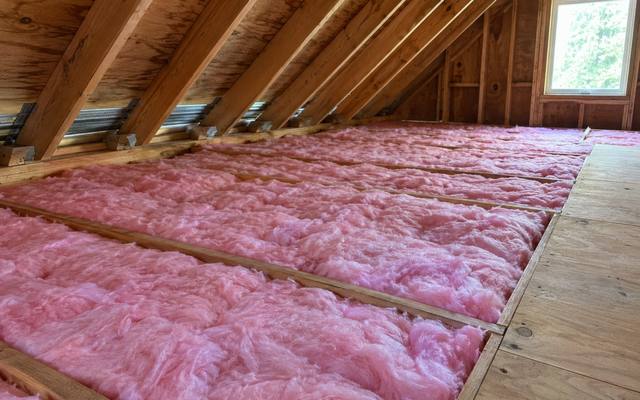 Pink fibreglass batts filling an attic beside a plywood walkway