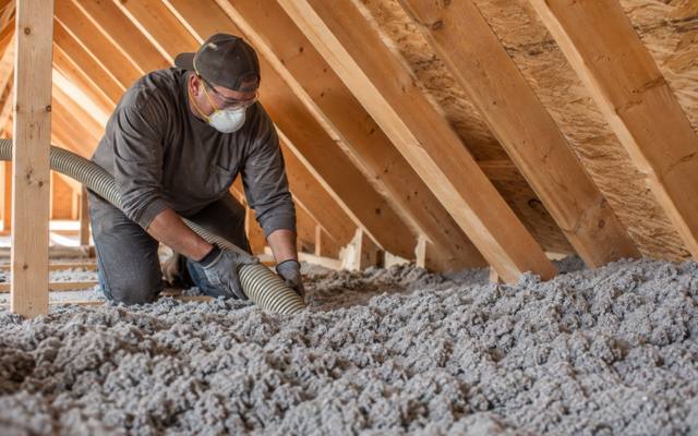 Installer blowing grey cellulose insulation across an attic floor in Orléans